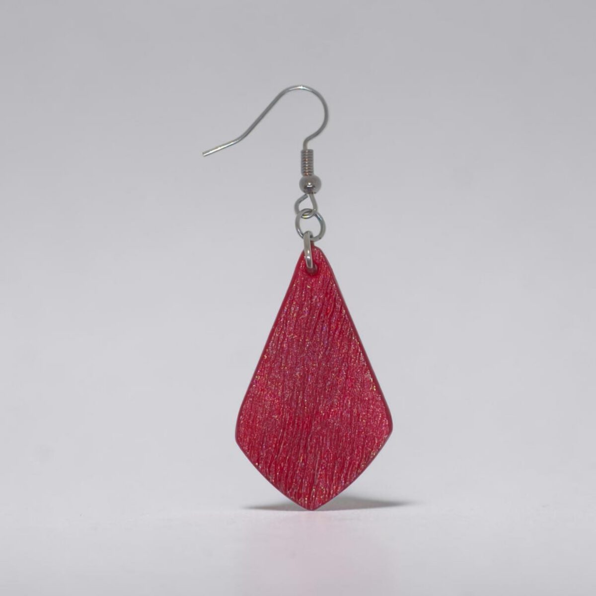 Boucle d'oreille forme larme en cuir teinture rouge, finition griffée, vue de face, suspendue à une boucle argentée, fond design