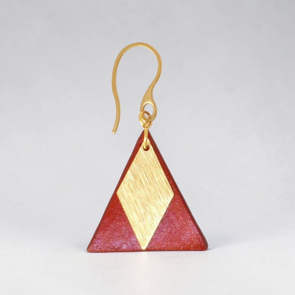 Boucle d'oreille forme triangulaire en cuir teinture cognac, finition lisse et pendant losange doré brossé, vue de face, suspendue à une boucle dorée, fond gris