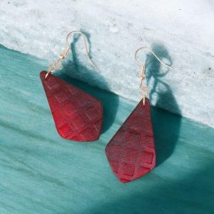 Boucles d'oreilles forme larme en cuir teinté rouge, texturage carrés et finition vieillie, vues de face, suspendues à des boucles argentées, fond pierre design