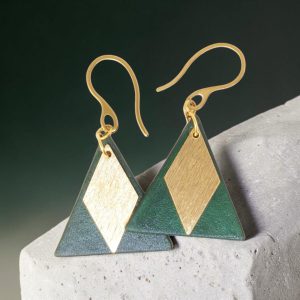 Boucles d'oreilles forme triangulaire en cuir teinture vert sombre, finition lisse et pendants losange dorés brossés vues de face se chevauchant, suspendues à des boucles dorées sur pierre