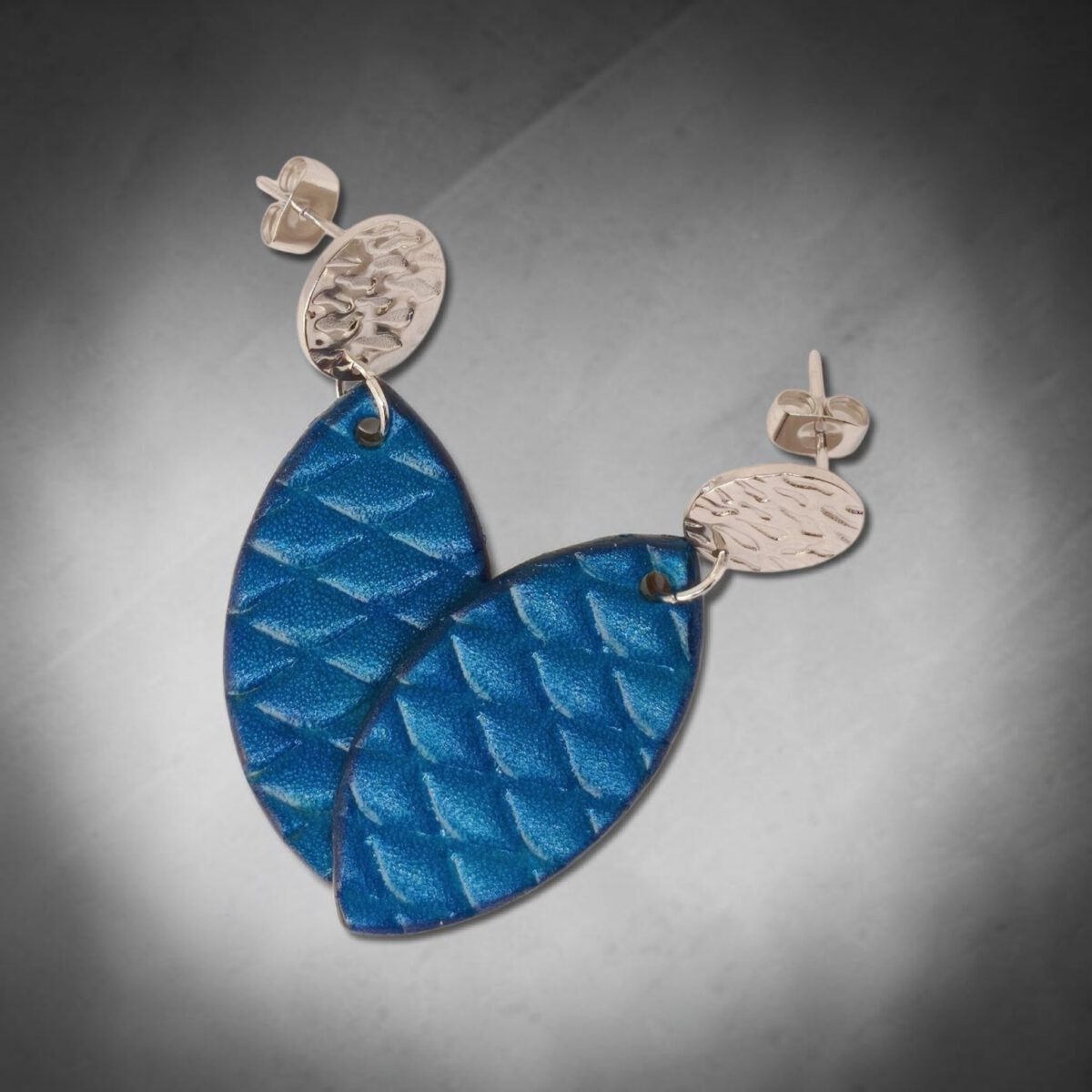 Boucles d'oreilles forme poisson en cuir teinture bleu, texturage poisson large, vues de face se chevauchant, suspendues à des boucles argentées sur dégradé