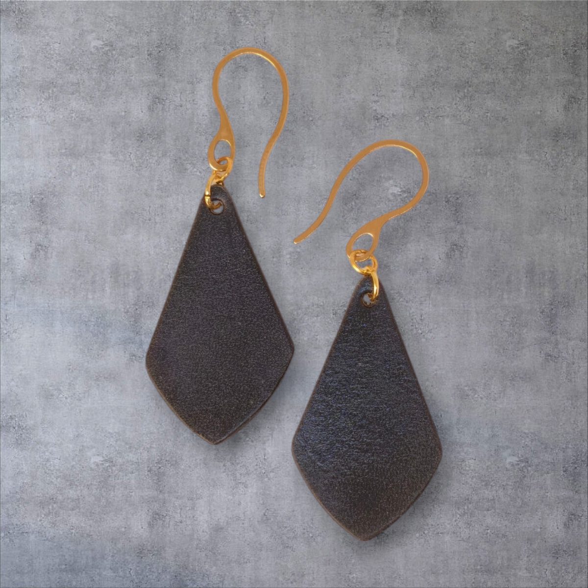 Boucles d'oreilles forme larme en cuir teinture noir charbon, finition lisse, vues de face, suspendues à des boucles dorées sur fond gris