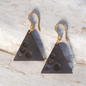 Boucles d'oreilles forme triangulaire en cuir teinture noire, finition lisse et ses trous, vues de face, suspendues à des boucles dorées sur pierre