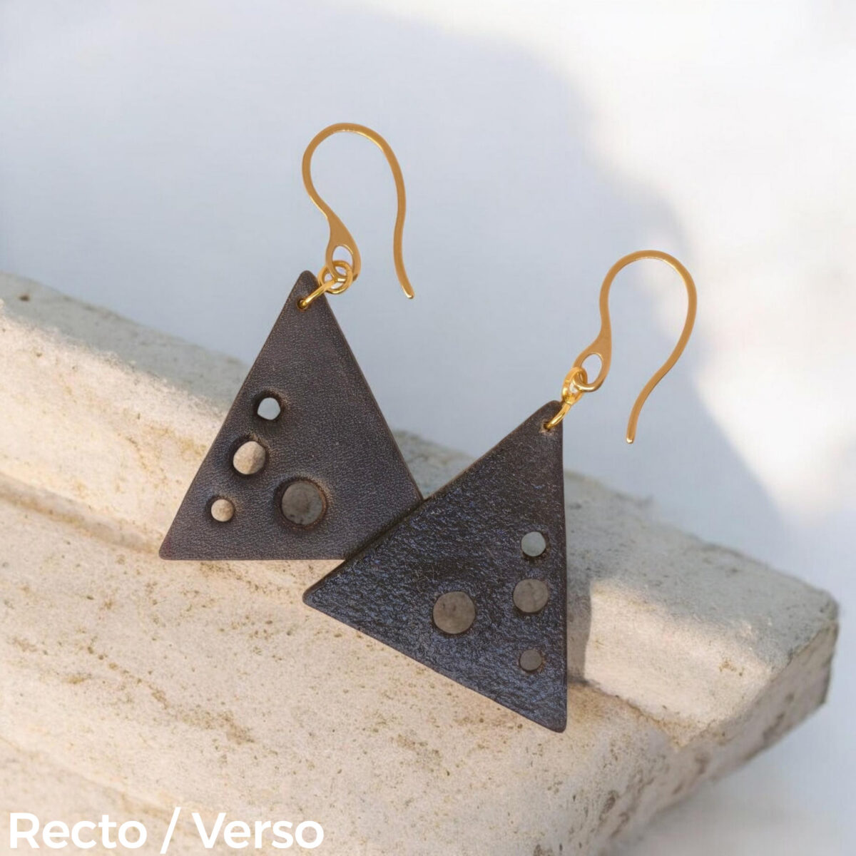 Boucles d'oreilles forme triangulaire en cuir teinture noire, finition lisse et ses trous, vues recto - verso se chevauchant, suspendues à des boucles dorées