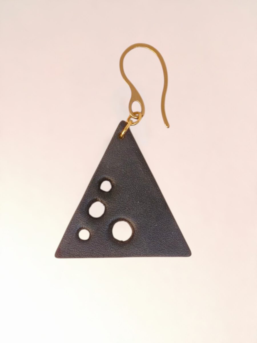 Boucle d'oreille forme triangulaire en cuir teinture noire, finition lisse et ses trous, vue de face, suspendue à une boucle dorée, fond dégradé