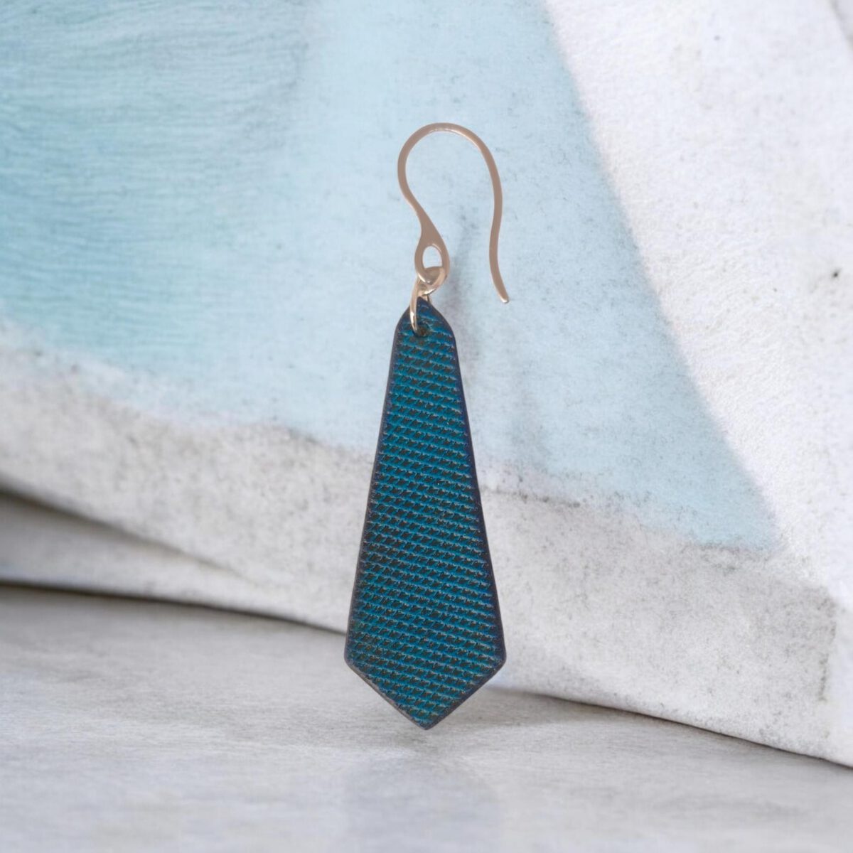 Boucle d'oreille en cuir teinte bleue, vue de face, suspendue à une boucle argentée fond design