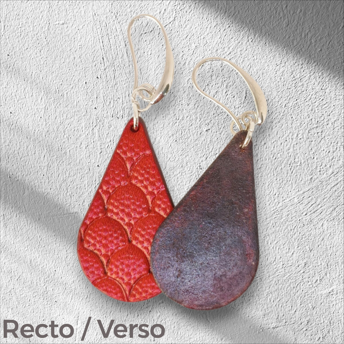 Boucles d'oreilles forme goutte d'eau en cuir teinture rouge, estampages au matoir écailles de dragon, vues recto - verso se chevauchant, suspendues à des boucles argentées sur crépi