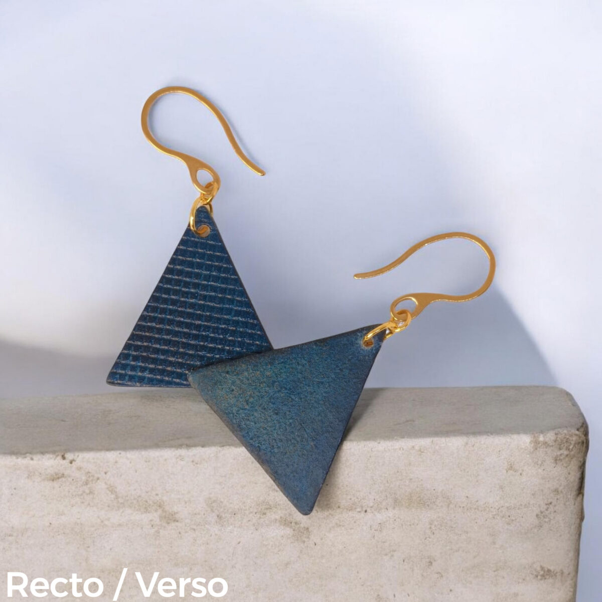 Boucles d'oreilles forme triangulaire en cuir teinture bleue, texturage quadrillage, vues recto - verso se chevauchant, suspendues à des boucles dorées sur pierre