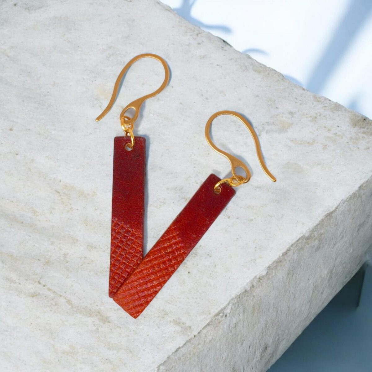 Boucles d'oreilles rectangulaires en cuir teinté cognac et acajou, finition mi-lisse mi-quadrillage , vues de face se chevauchant, suspendues à des boucles dorées sur pierre