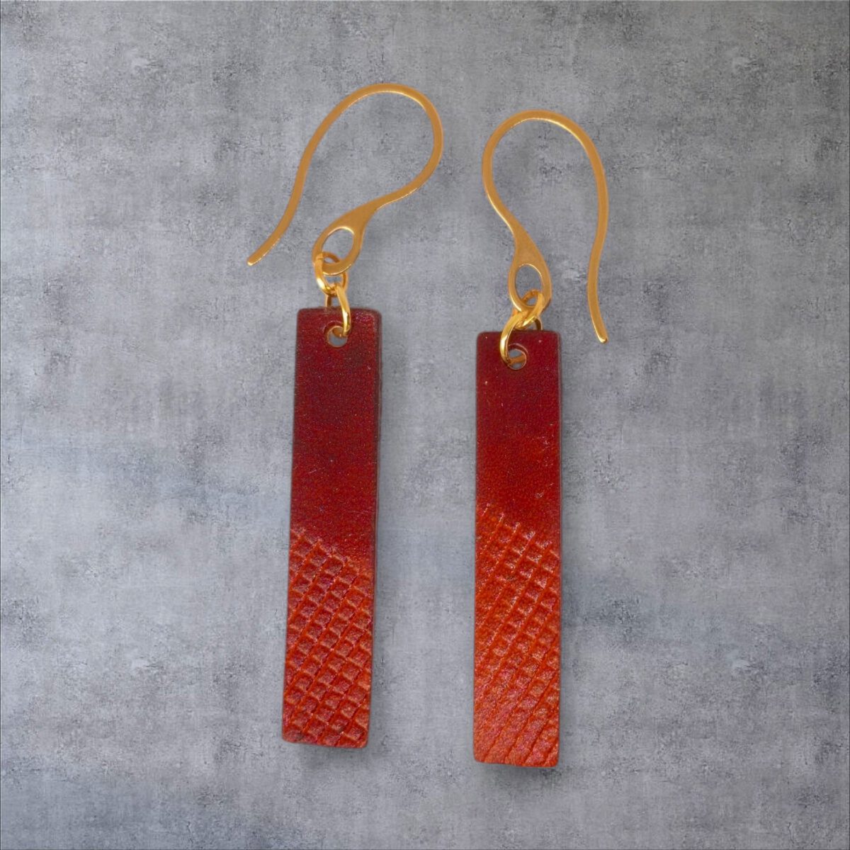 Boucles d'oreilles rectangulaires en cuir teinté cognac et acajou, finition mi-lisse mi-quadrillage , vues de face, suspendues à des boucles dorées sur fond gris