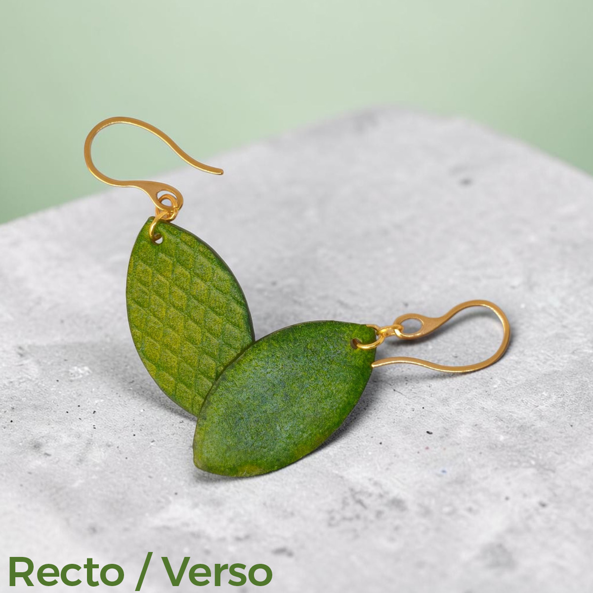 Boucles d'oreilles forme poisson en cuir teinture vert forêt, texturage gros quadrillage, vues recto - verso se chevauchant, suspendues à des boucles dorées sur béton