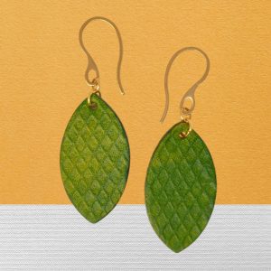 Boucles d'oreilles forme poisson en cuir teinture vert forêt, texturage gros quadrillage, vues de face, suspendues à des boucles dorées sur tissu bicolore