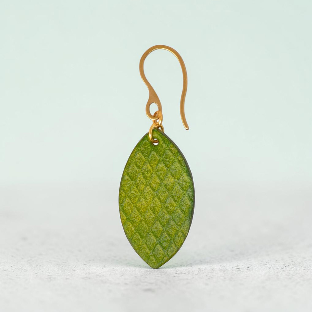 Boucles d'oreilles forme poisson en cuir teinture vert forêt, texturage gros quadrillage, vues de face, suspendues à des boucles dorées sur pierre