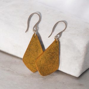 Boucles d'oreilles forme larme en cuir teinture jaune, finition lime vieillie, vues de face se chevauchant, suspendues à des boucles argentées, sur pierre