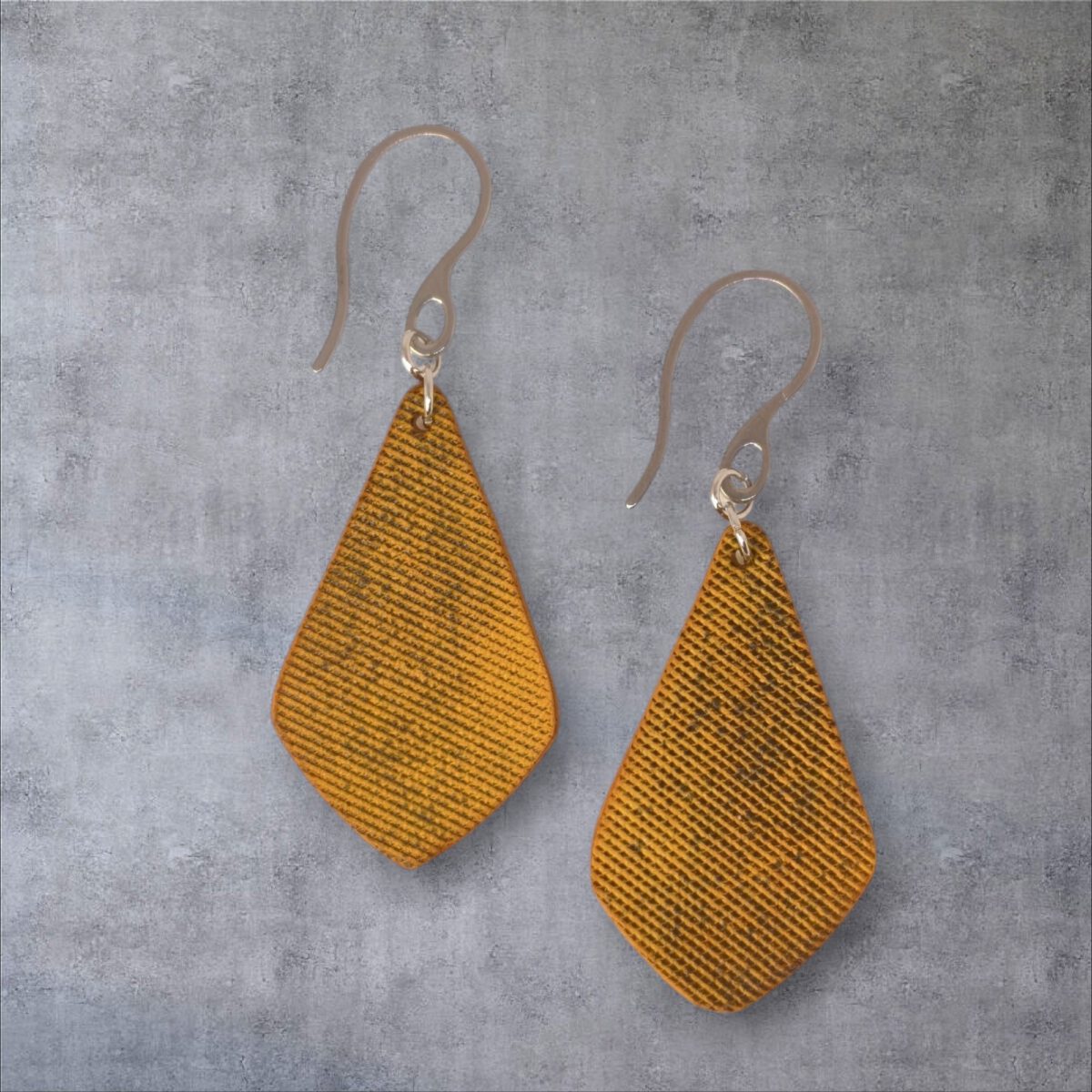Boucles d'oreilles forme larme en cuir teinture jaune, finition lime vieillie, vues de face, suspendues à des boucles argentées, fond gris