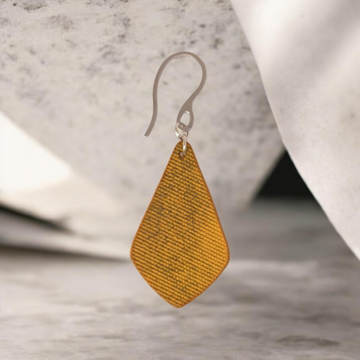 Boucle d'oreille forme larme en cuir teinture jaune, finition lime vieillie, vue de face, suspendue à une boucle argentée, fond design
