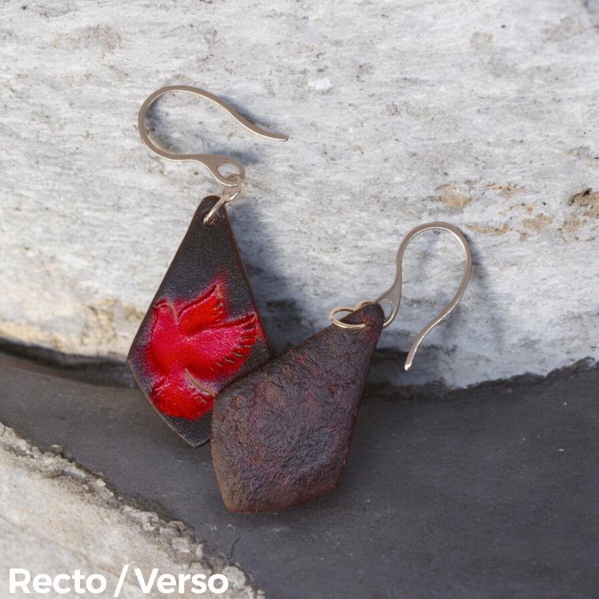Boucles d'oreilles en cuir teintées en rouge et noir, vues recto - verso se chevauchant, suspendues à des crochets argentés sur pierre