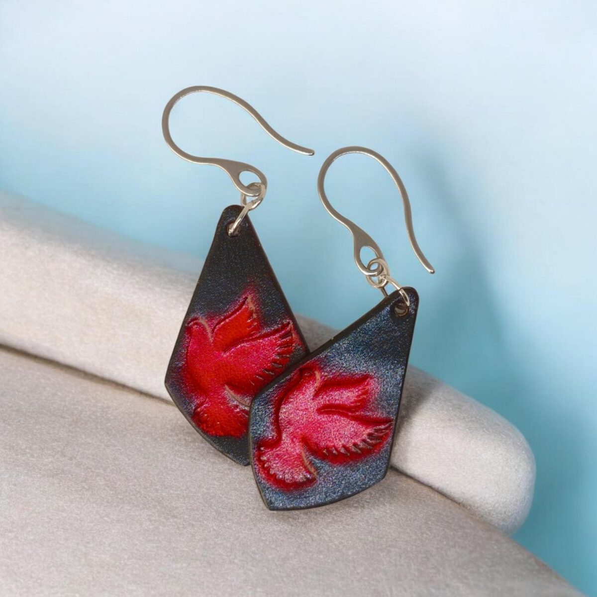 Boucles d'oreilles en cuir teintées en rouge et noir, vues de face se chevauchant, suspendues à des crochets argentés, fond design