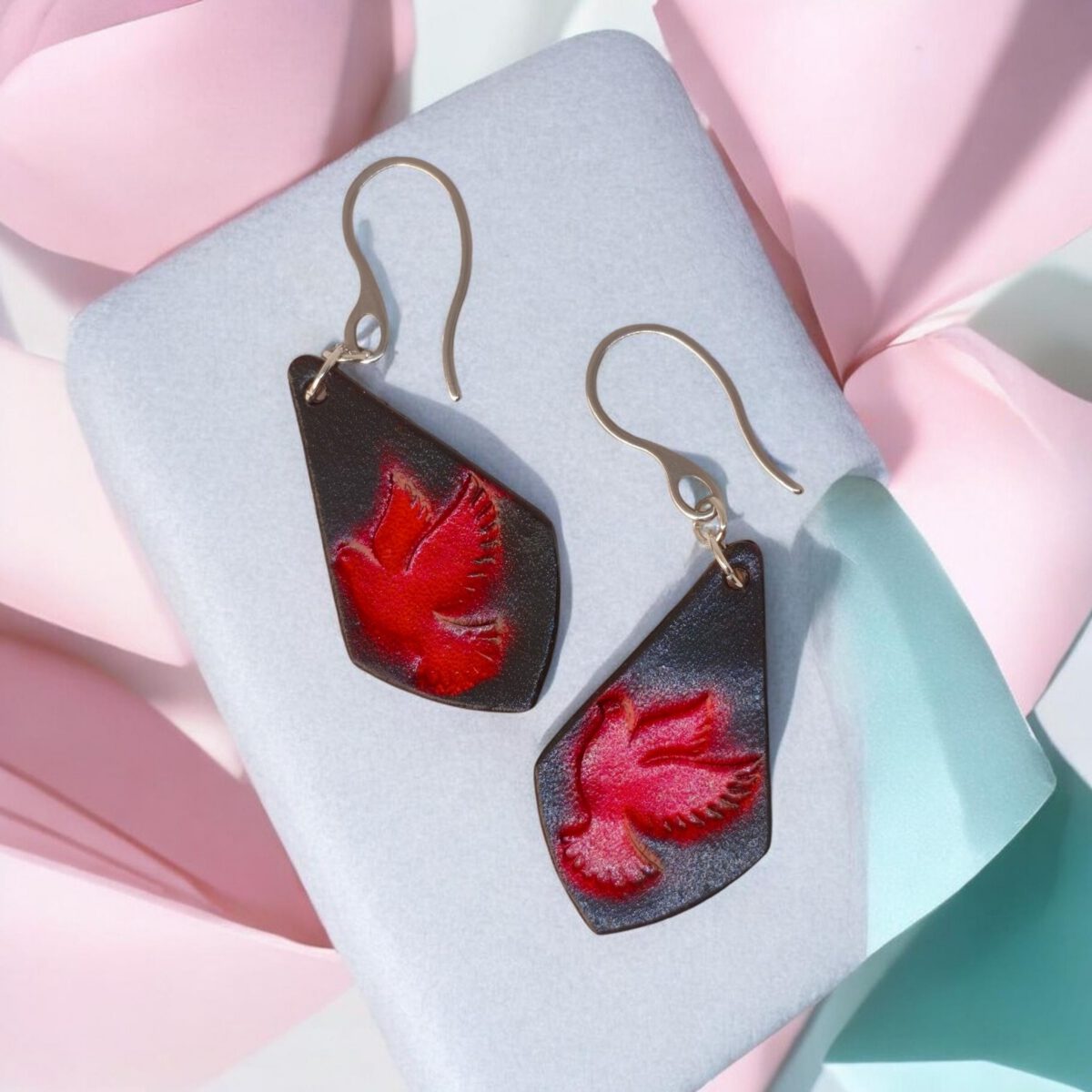 Boucles d'oreilles en cuir teintées en rouge et noir, vues de face, suspendues à des crochets argentés sur fond design