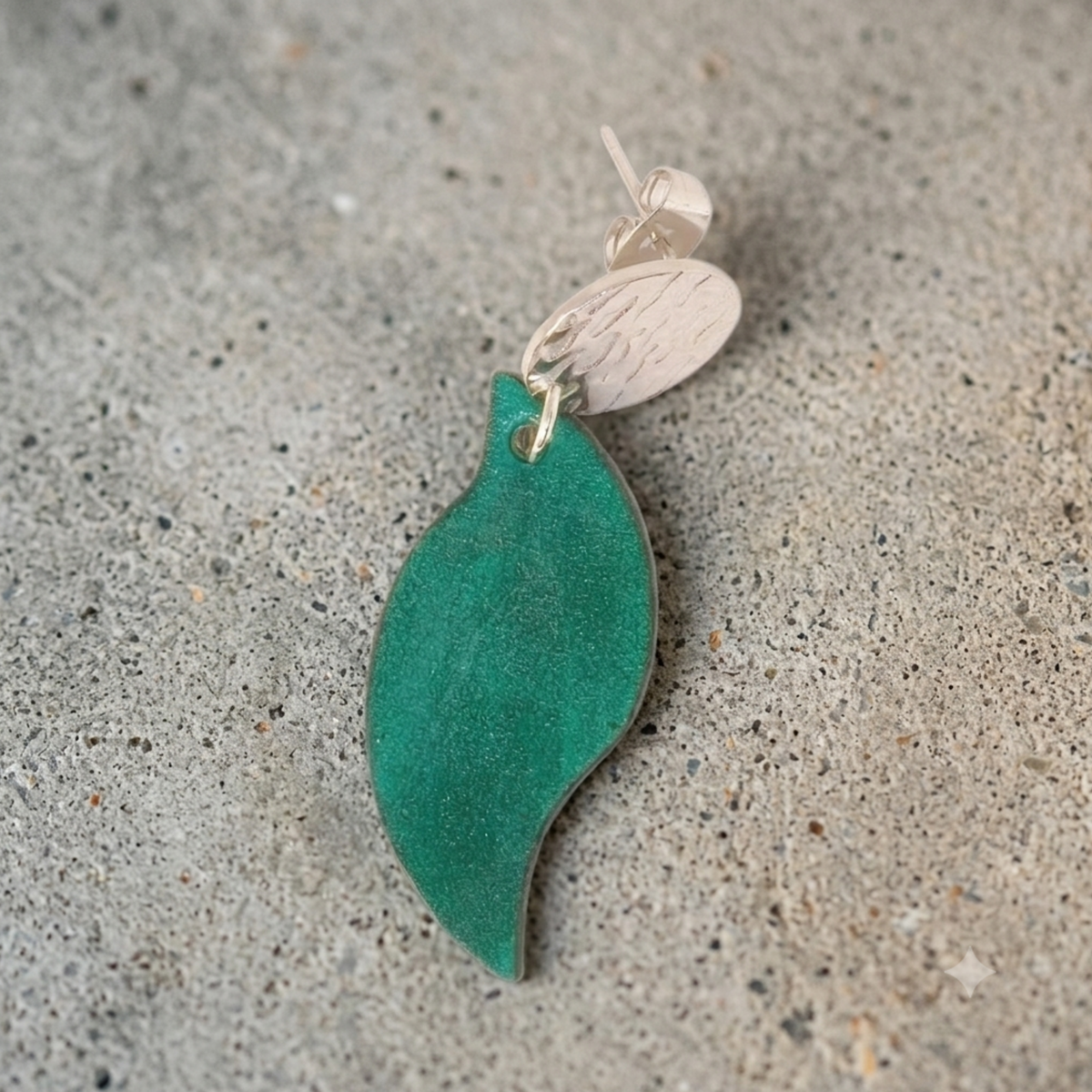 Boucle d'oreille forme feuille asymétrique en cuir teinté vert d'eau, finition lisse, vue de face, suspendue à une boucle argentée, sur pierre