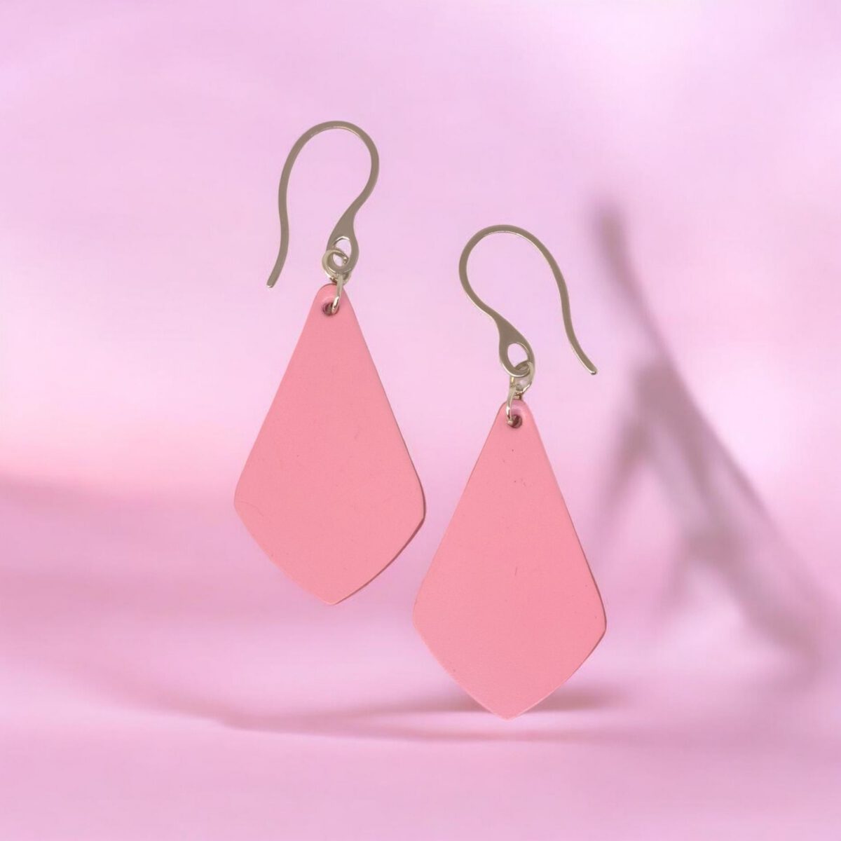 Boucles d'oreilles forme larme en cuir rose, finition lisse, vues de face, suspendues à des boucles argentées, fond design