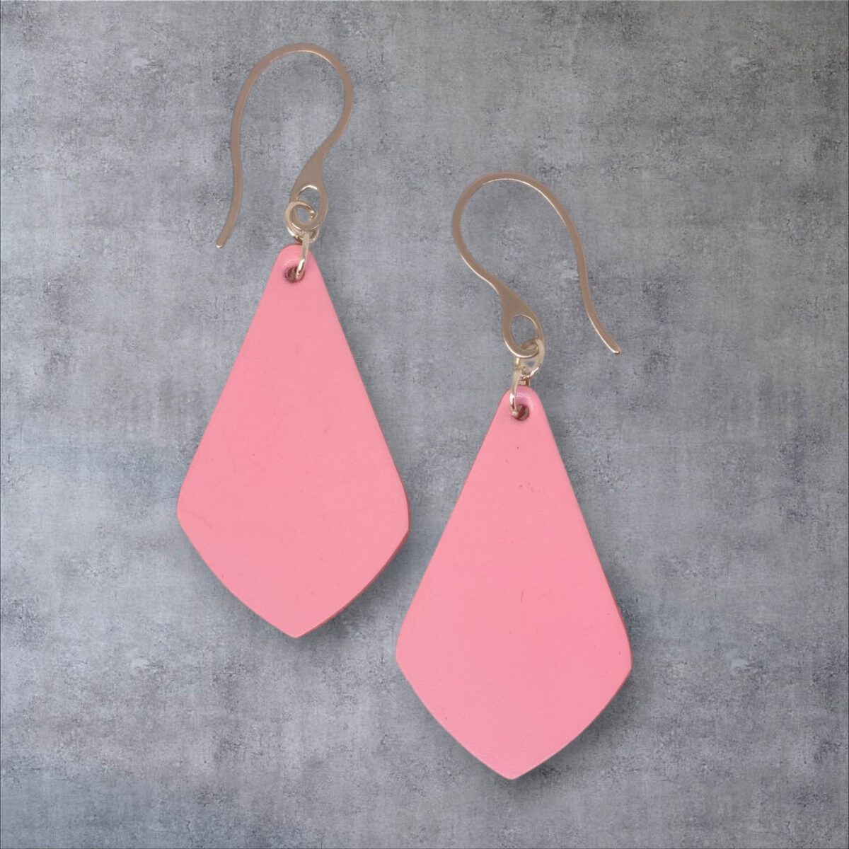 Boucles d'oreilles forme larme en cuir rose, finition lisse, vues de face, suspendues à des boucles argentées, fond gris