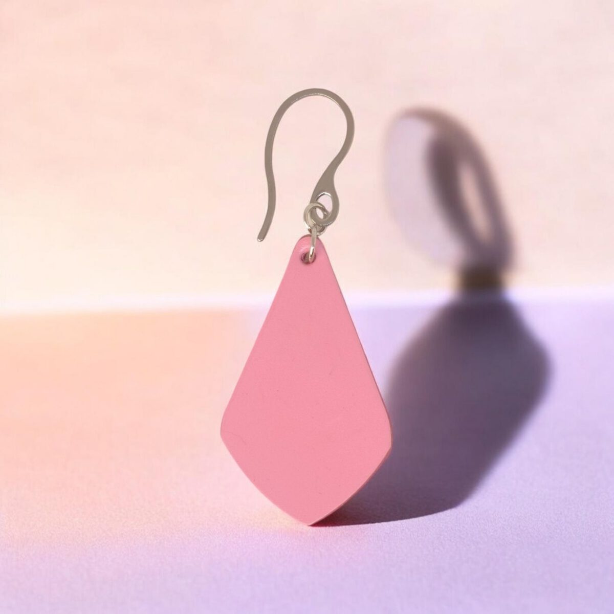 Boucle d'oreille forme larme en cuir rose, finition lisse, vue de face, suspendue à une boucle argentée, fond design