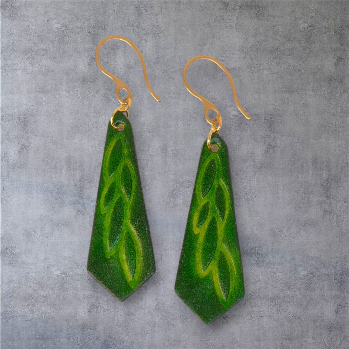 Boucles d'oreilles cravates en cuir teinté vert forêt, estampage feuille longue, vues de face, suspendues à des boucles dorées, fond gris