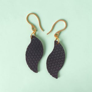 Boucles d'oreilles forme feuille asymétrique en cuir teinté bleu nuit, texturage en tannerie, vues de face, suspendues à des boucles dorées sur fond design