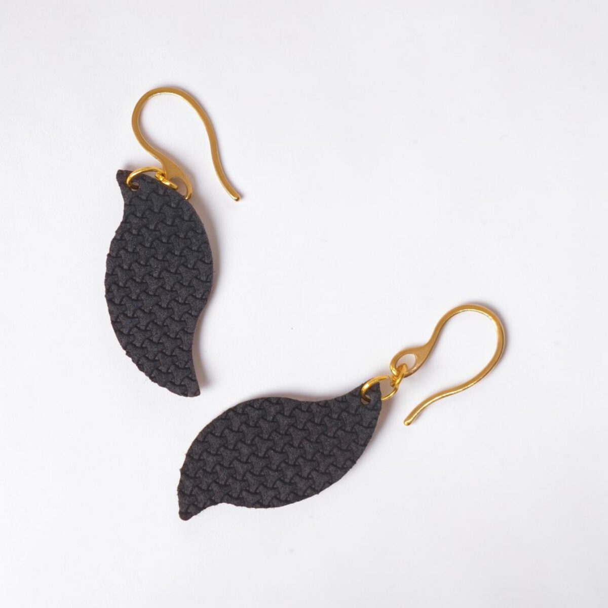 Boucles d'oreilles forme feuille asymétrique en cuir teinté bleu nuit, texturage en tannerie, vues de face, suspendues à des boucles dorées sur fond blanc