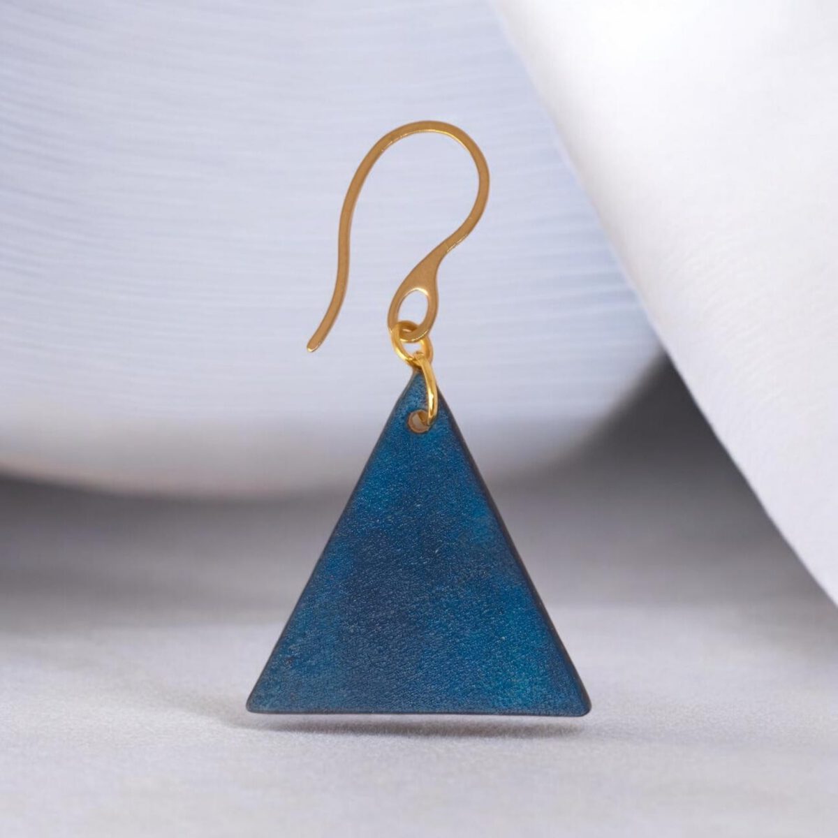 Boucle d'oreille forme triangulaire en cuir teinture bleue, finition lisse, vue de face, suspendue à une boucle dorée, fond design