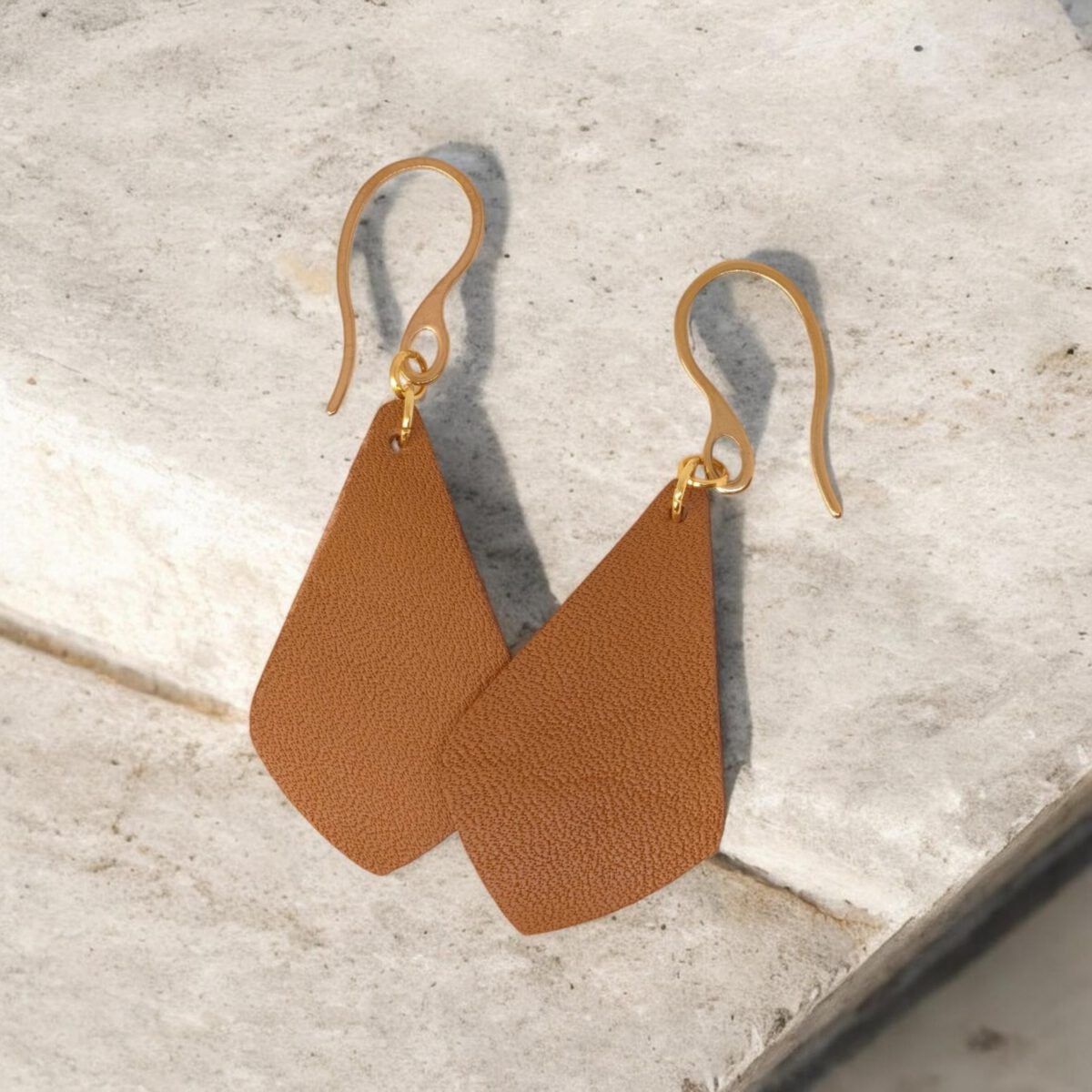 Boucles d'oreilles forme larme en cuir marron, finition léger grain, vues de face se chevauchant, suspendues à des boucles dorées sur pierre