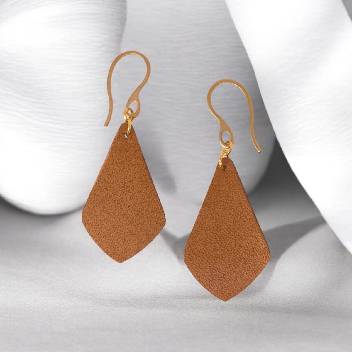 Boucles d'oreilles forme larme en cuir marron, finition léger grain, vues de face, suspendues à des boucles dorées sur fond design