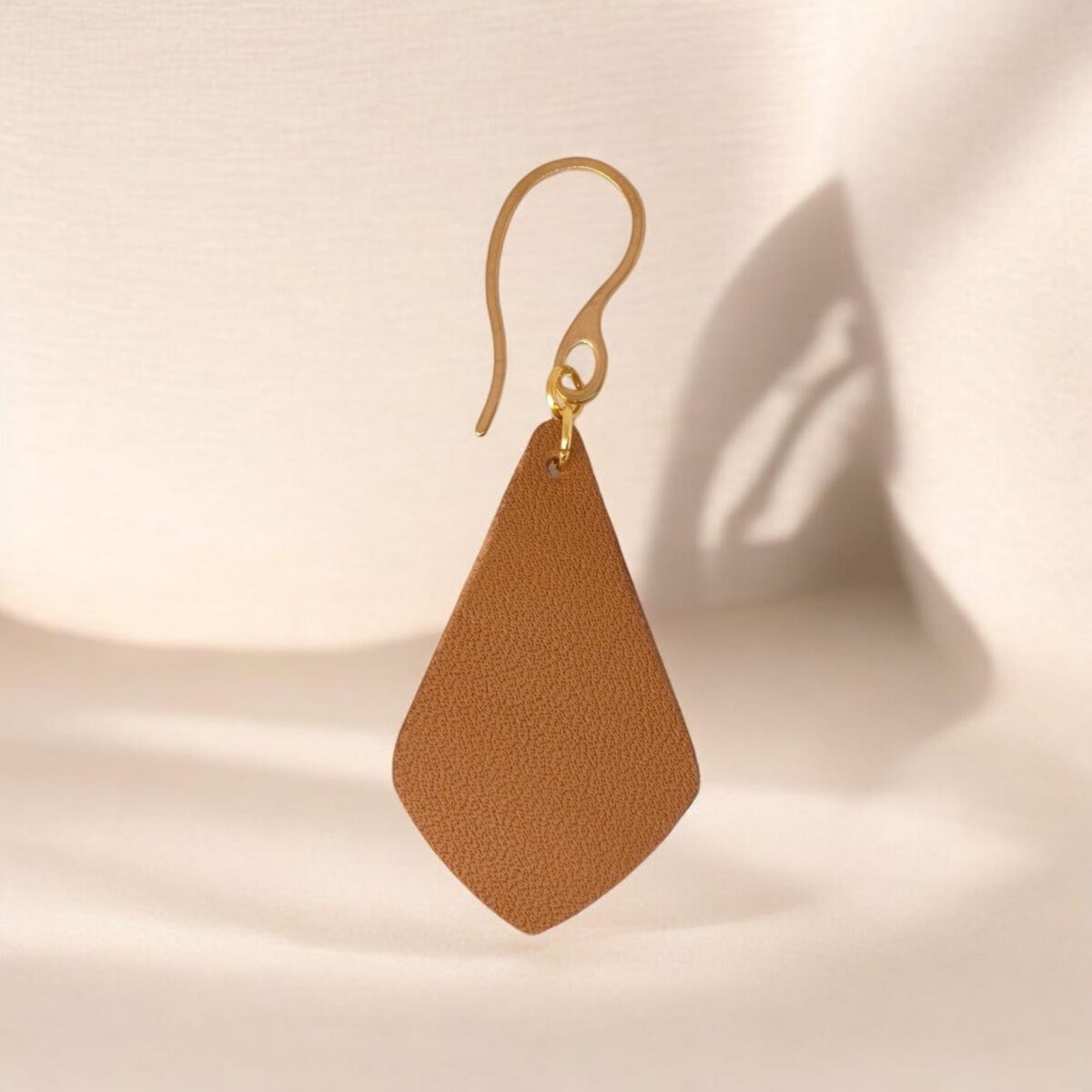 Boucle d'oreille forme larme en cuir marron, finition léger grain, vue de face, suspendue à une boucle dorée, fond design
