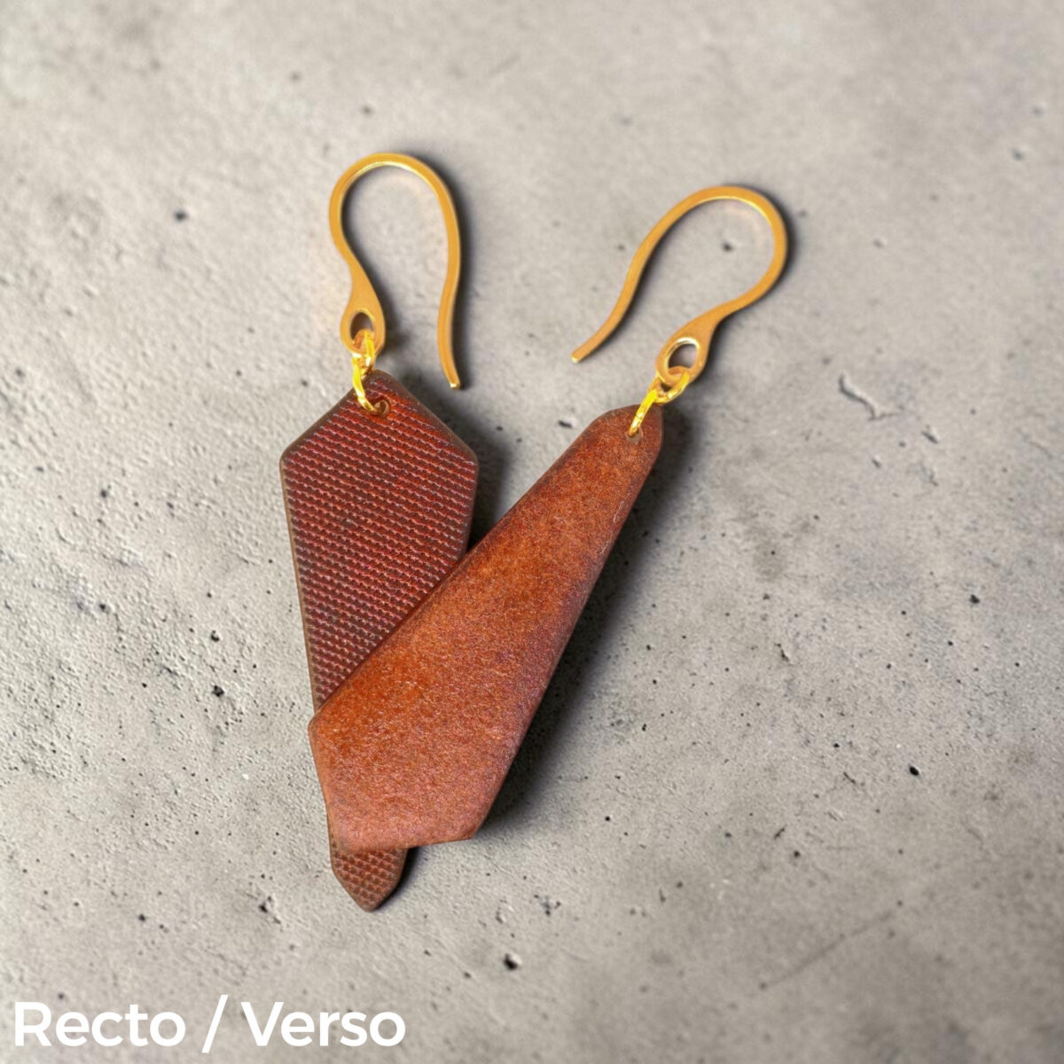 Boucles d'oreilles cravates asymétriques en cuir teinté cognac, finition lime vieillie, vues recto - verso se chevauchant, suspendues à des boucles dorées sur fond gris