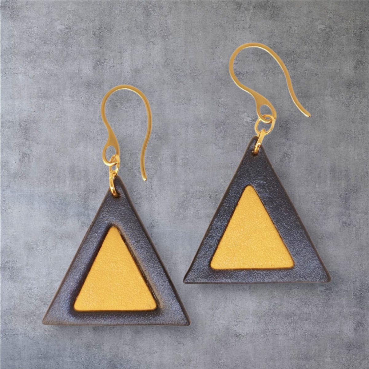 Boucles d'oreilles forme triangulaire double asymétrique en cuir teinture noire et jaune, finition lisse, vues de face, suspendues à des boucles dorées, fond gris