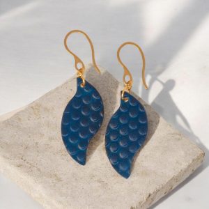 Boucles d'oreilles forme feuille asymétrique en cuir teinté bleu, texturage ronds, vues de face, suspendues à des boucles dorées sur pierre