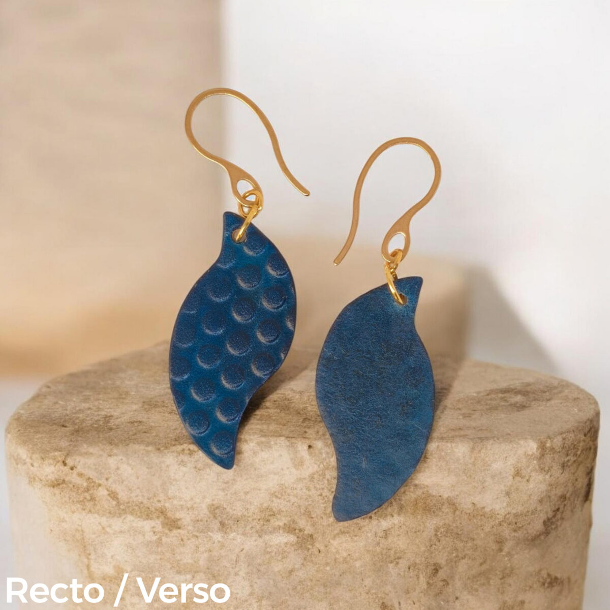 Boucles d'oreilles forme feuille asymétrique en cuir teinté bleu, texturage ronds, vues rectp - verso, suspendues à des boucles dorées sur pierre