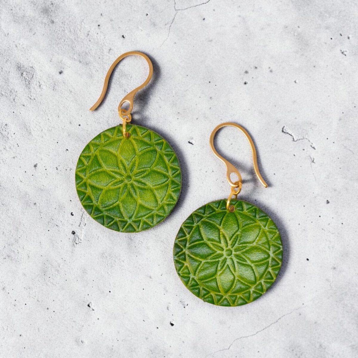 Boucles d'oreilles rondes en cuir teinté vert forêt, texturage fleur mandala, vues de face, suspendues à des boucles dorées sur béton