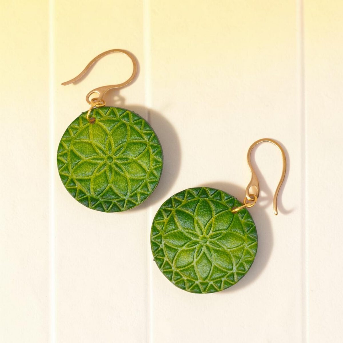 Boucles d'oreilles rondes en cuir teinté vert forêt, texturage fleur mandala, vues de face, suspendues à des boucles dorées sur fond clair