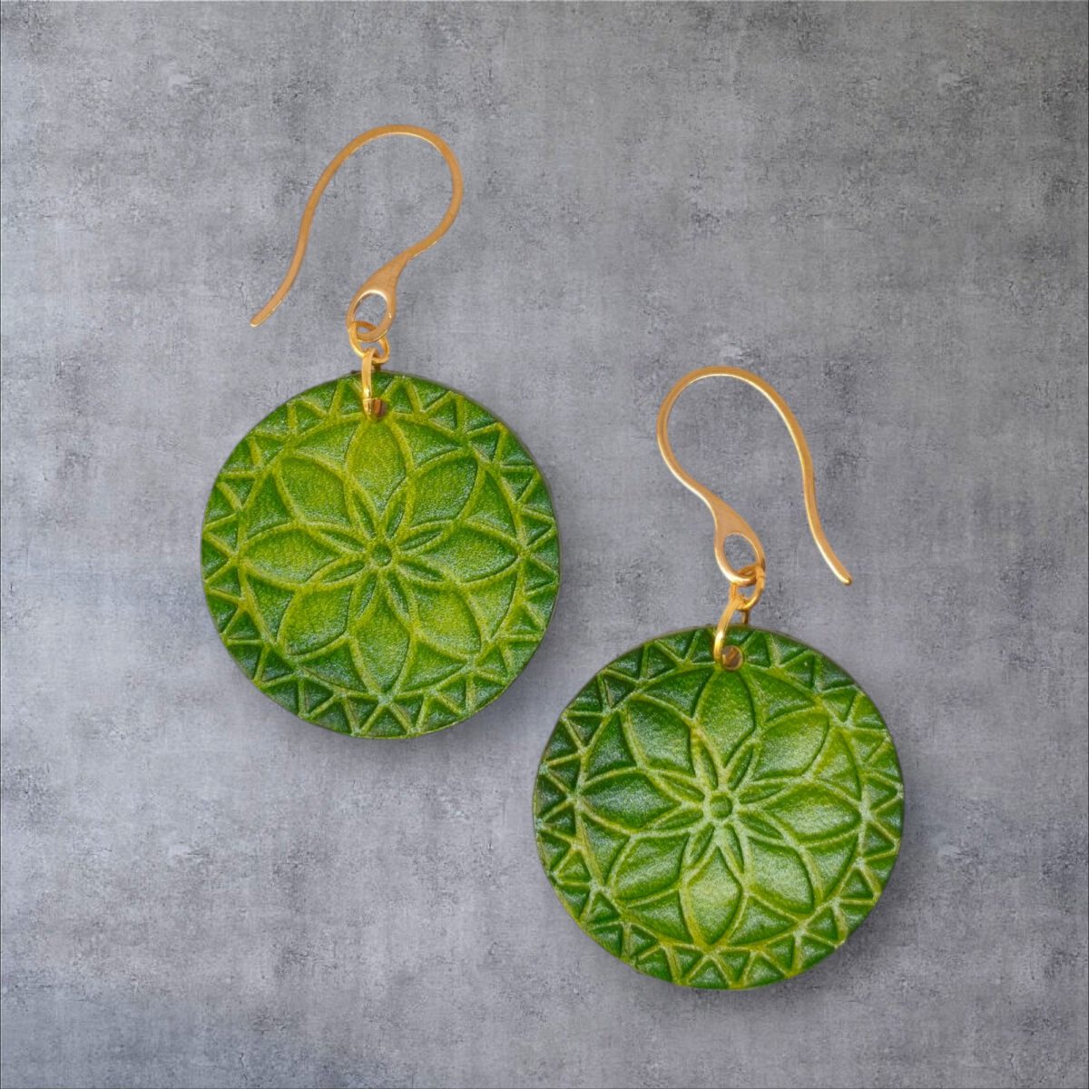 Boucles d'oreilles rondes en cuir teinté vert forêt, texturage fleur mandala, vues de face, suspendues à des boucles dorées sur fond gris