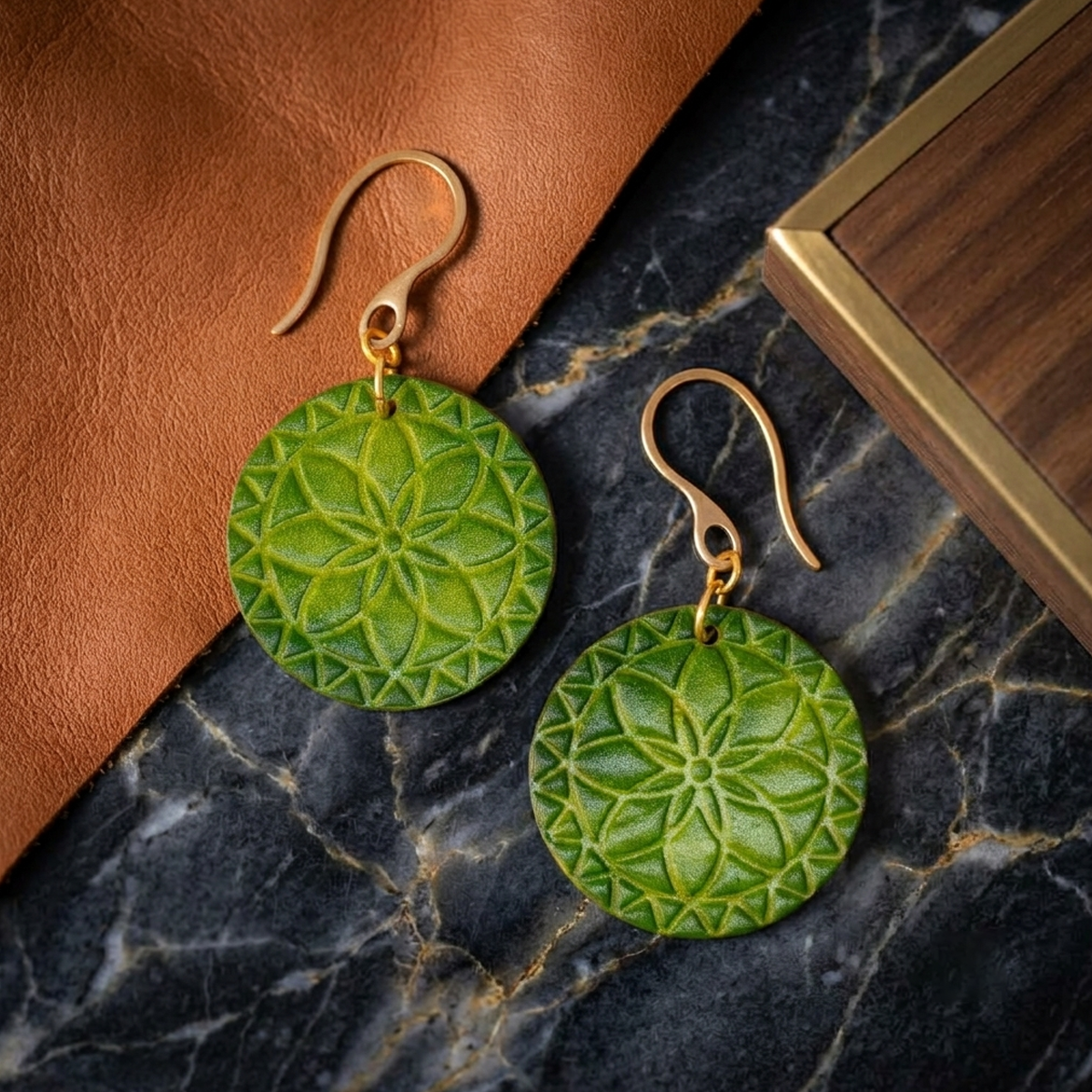 Boucles d'oreilles rondes en cuir teinté vert forêt, texturage fleur mandala, vues de face, suspendues à des boucles dorées sur marbre noir
