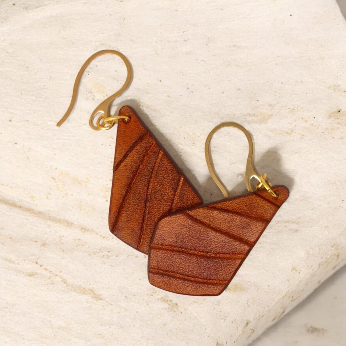 Boucles d'oreilles en cuir teinté cognac, vues de face se chevauchant, suspendues à des crochets dorés