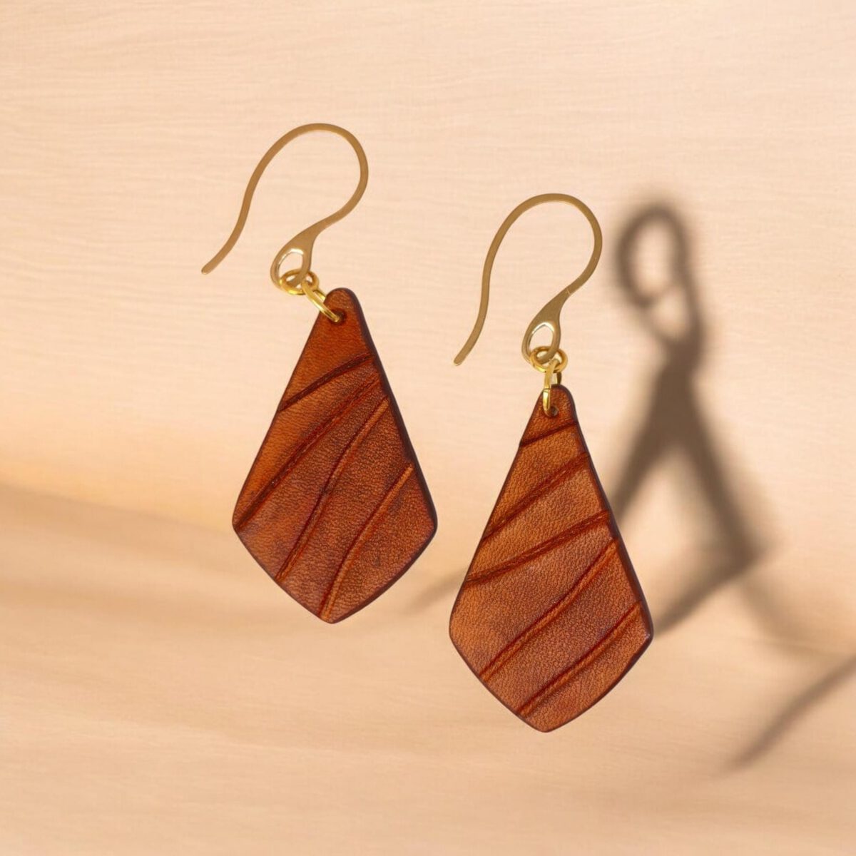 Boucles d'oreilles en cuir teinté cognac, vues de face parallèles, suspendues à des crochets dorés