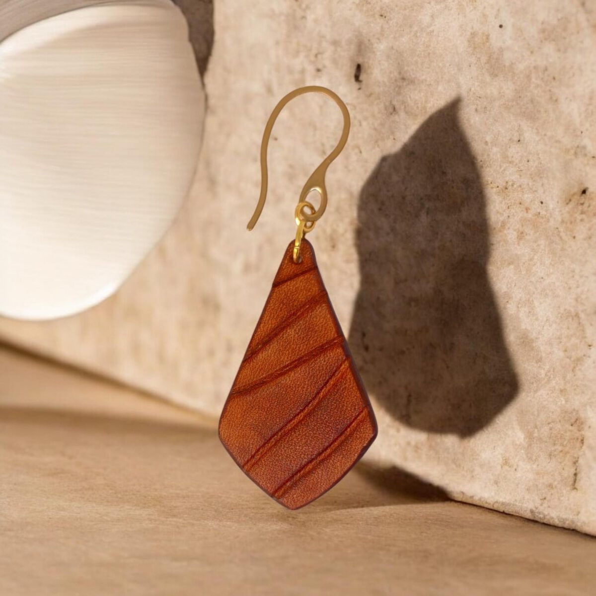 Boucle d'oreille en cuir teinté cognac, vue de face, suspendue à un crochet doré