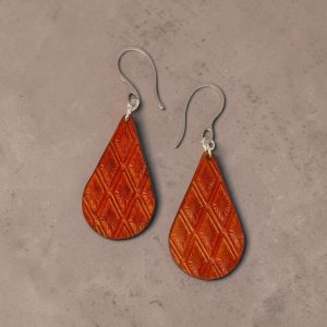 Boucles d'oreilles forme goutte d'eau en cuir teinture cognac, estampages au matoir losange, vues de face, suspendues à des boucles argentées sur fond design