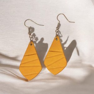 Boucles d'oreilles forme larme en cuir teinture jaune, finition galet, vues de face, suspendues à des boucles argentées sur tissu