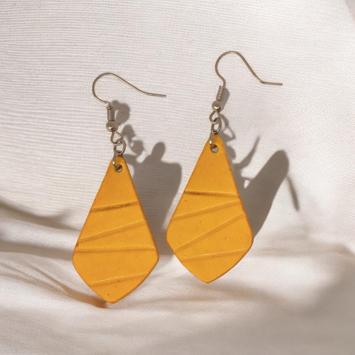 Boucles d'oreilles forme larme en cuir teinture jaune, finition galet, vues de face, suspendues à des boucles argentées sur tissu