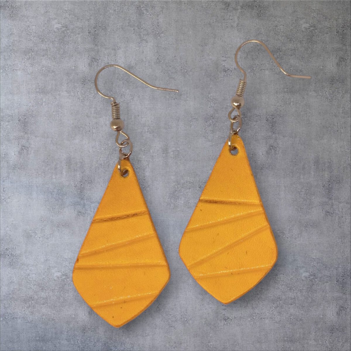 Boucles d'oreilles forme larme en cuir teinture jaune, finition galet, vues de face, suspendues à des boucles argentées sur fond gris