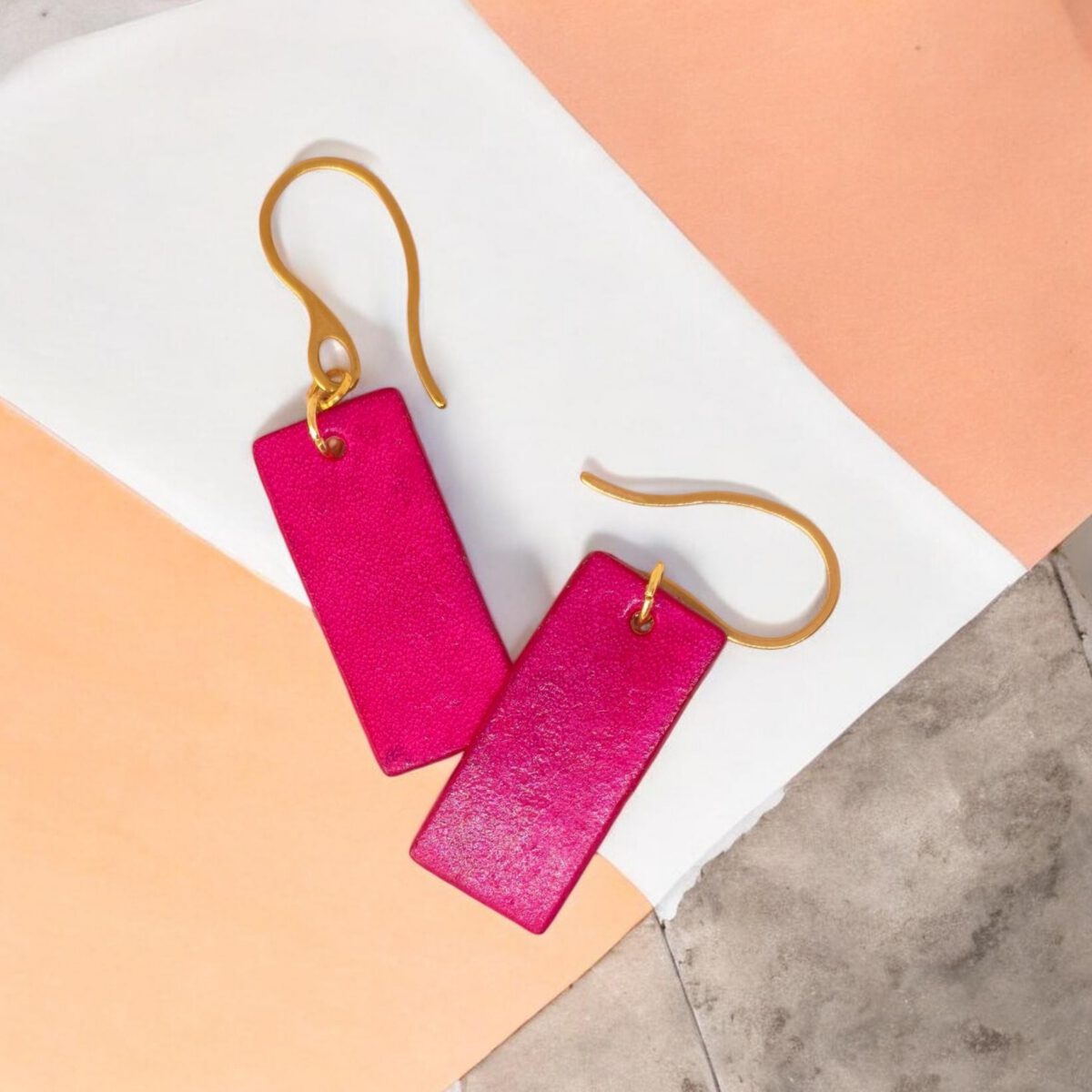 Boucles d'oreilles en cuir teintées en fuschia très girly et vives, vues de face se chevauchant, suspendues à des crochets dorés